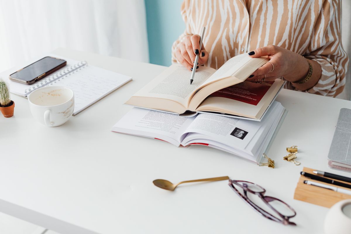 Pessoa lendo e grifando um livro sobre uma mesa, em ambiente calmo e organizado
